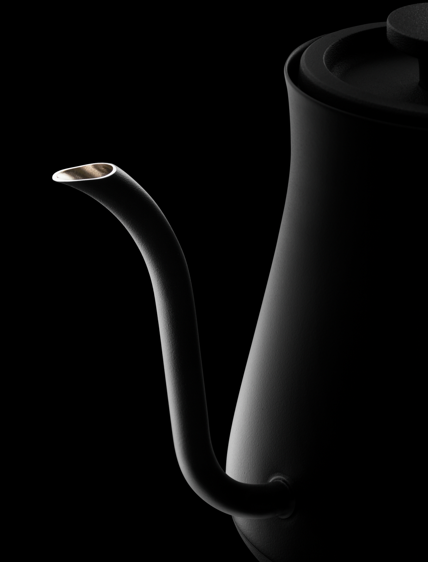 A dramatic close-up of the spout of a black BALMUDA kettle, lit against a black background.